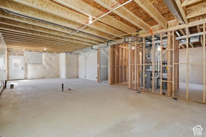 Unfinished basement featuring exposed wood framing, concrete flooring, and an exterior door with a window