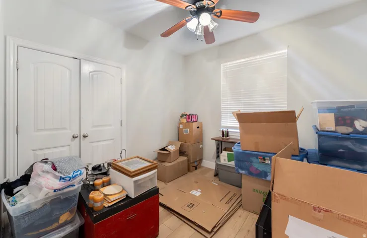 Wood-finish flooring, white walls, ceiling fan with integrated lighting, and a window with blinds