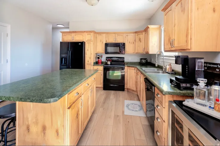 Kitchen featuring wood-finish flooring, light wood cabinetry, dark countertops, black appliances, and a built-in kitchen island