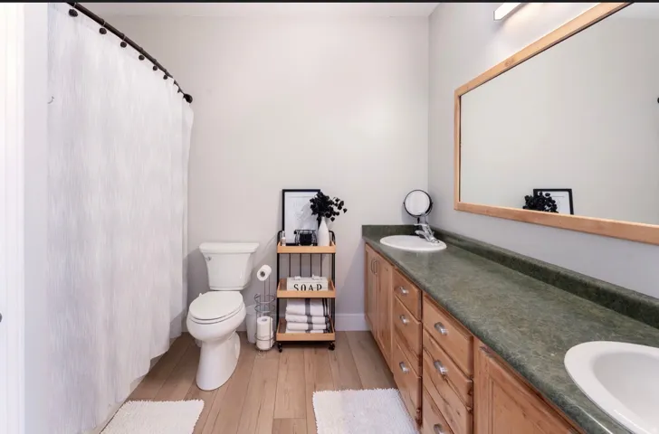 Dual basin vanity with wood-finish cabinetry, a framed mirror, and wood-finish flooring