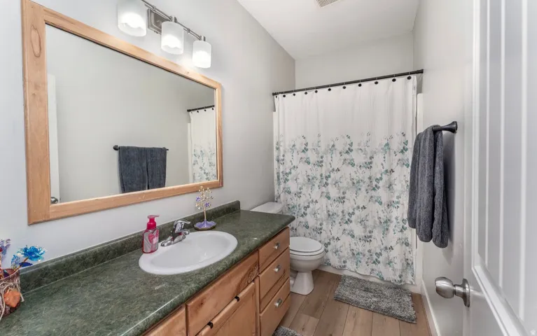Wood-finish flooring, a vanity with wood cabinetry and a dark countertop, a framed mirror, and a full bathtub with shower