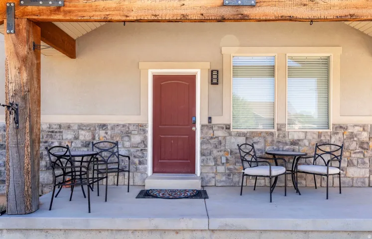 Covered concrete porch featuring a wood beam and column, stone veneer siding, and a paneled front door