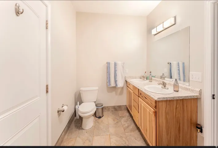 Dual vanity with integrated sinks, granite-look countertop, wood-finish cabinetry, and tiled flooring