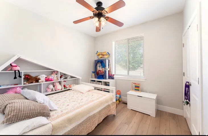 Recessed window with blinds, wood-finish flooring, and a ceiling fan with integrated lighting