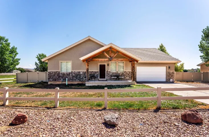 Stucco exterior with stone accenting, covered entry porch with exposed wood beams, attached garage, and a front yard with a decorative fence