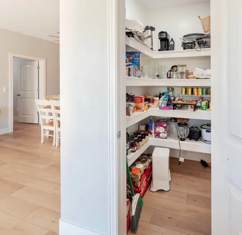 Walk-in pantry featuring built-in shelving, light wood-finish flooring, and white walls