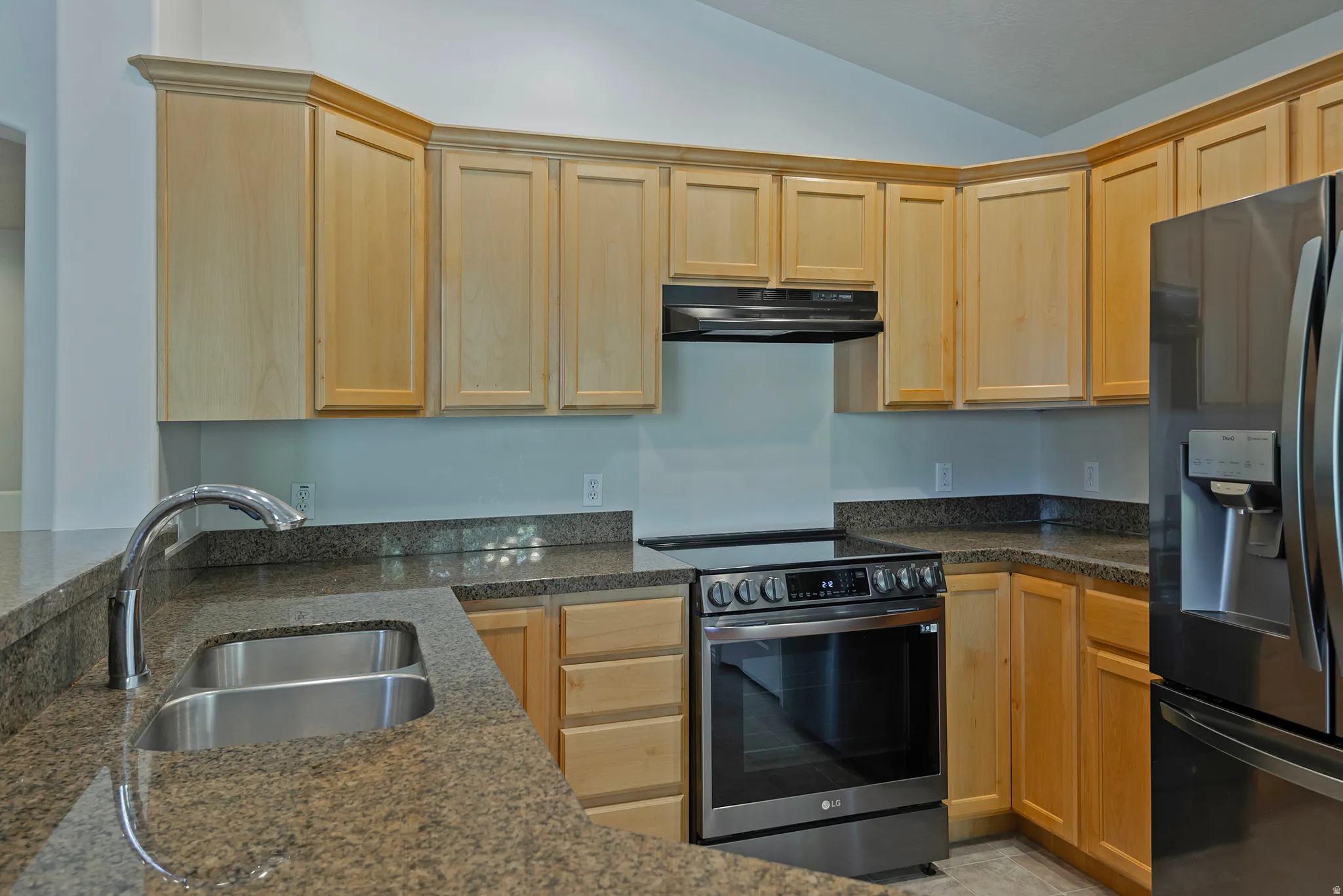 Light wood cabinetry, stainless steel double basin sink, curved countertop with breakfast bar, stainless steel range, and stainless steel refrigerator