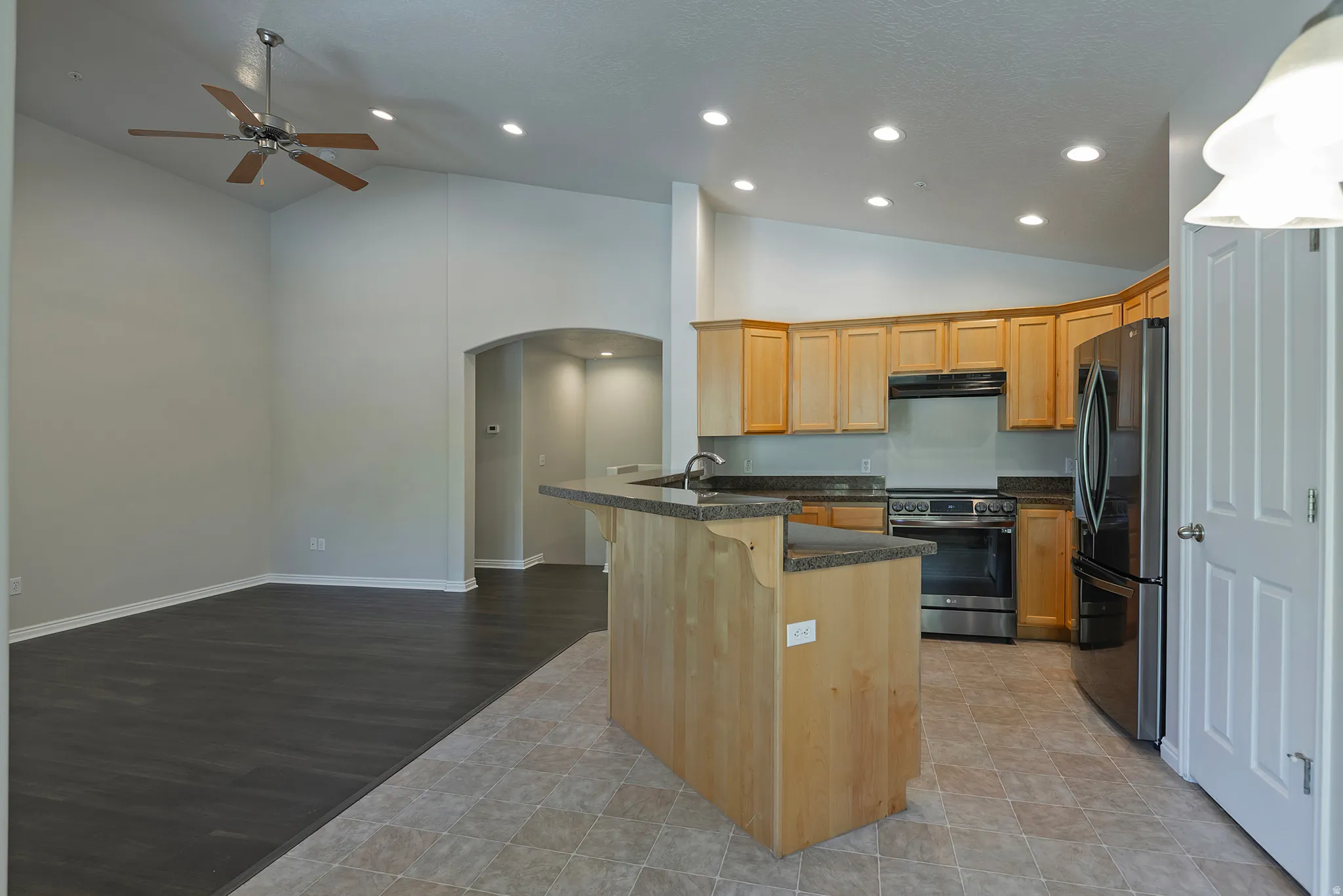 Vaulted ceilings, wood-finish flooring, recessed lighting, arched doorway, and a kitchen featuring wood cabinetry