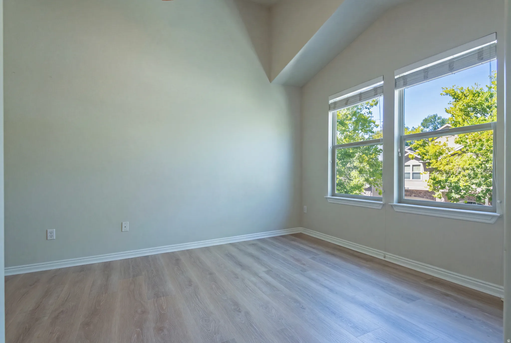 Vaulted ceiling, wood-finish flooring, white baseboards, and two large windows
