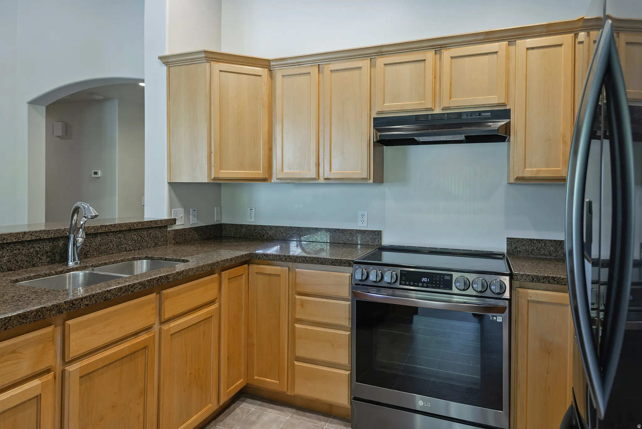 Kitchen featuring light wood cabinetry, stone countertops, a stainless steel electric range, and a double basin sink with a high-arc faucet