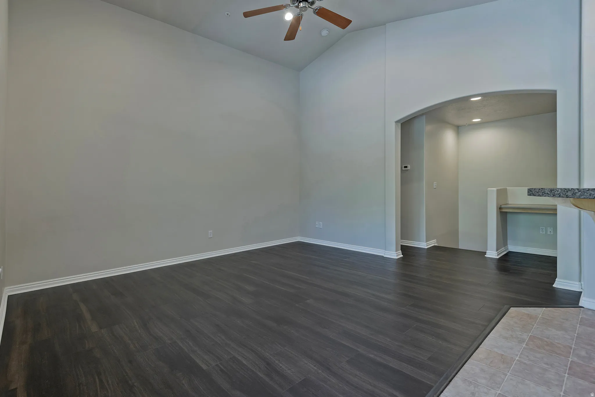 Vaulted ceiling with a ceiling fan, dark wood-finish flooring, arched doorway, recessed lighting, and a built-in desk area with a stone-finish countertop