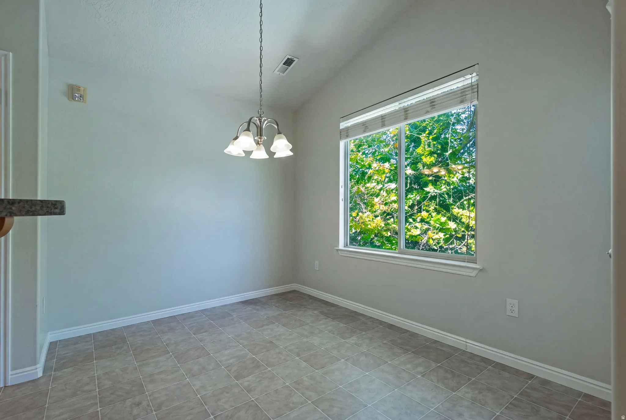 Vaulted ceiling with an attached chandelier, tiled flooring, and a large window
