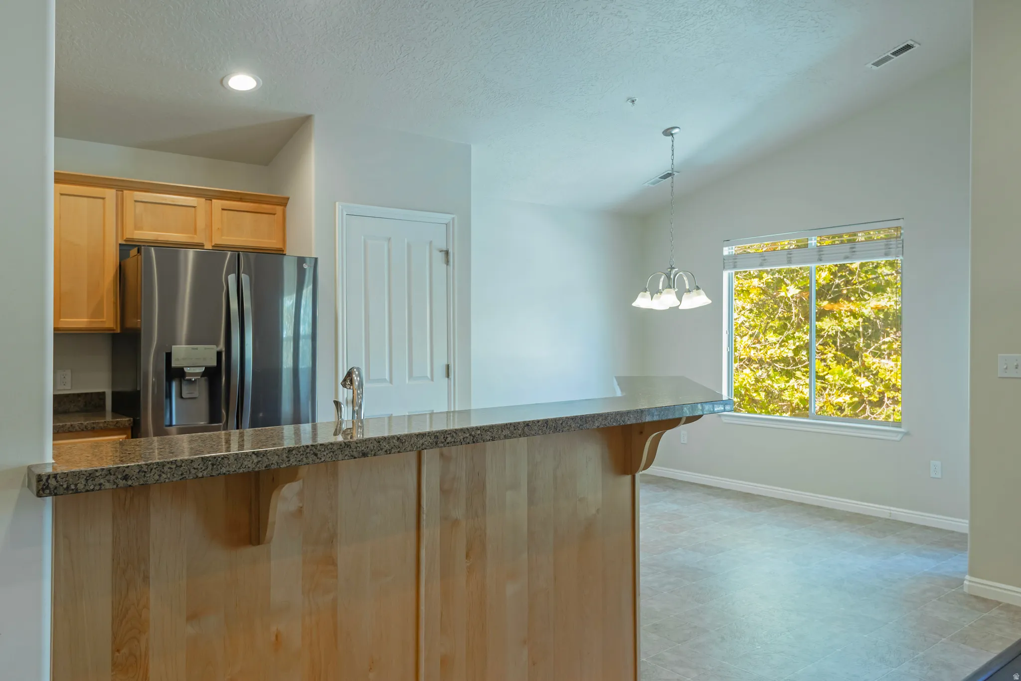Kitchen featuring wood cabinetry, stainless steel refrigerator, and granite-style countertops