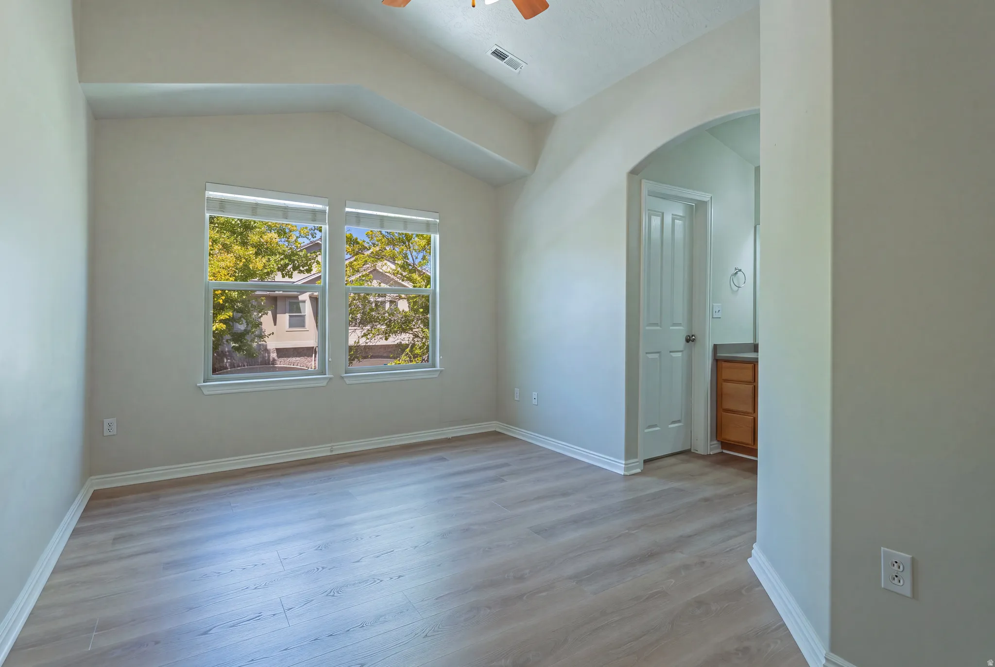Vaulted ceiling, two large windows, wood-finish flooring, arched doorway, and a vanity with a wood-finish cabinet