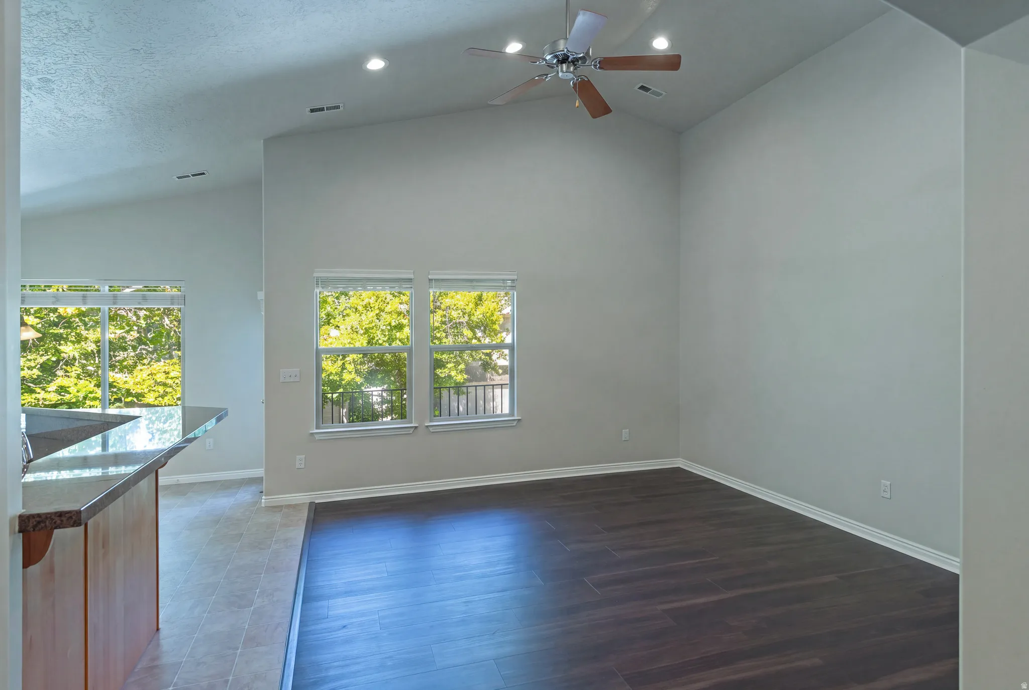 Vaulted ceilings, recessed lighting, wood-finish flooring, a ceiling fan, and a built-in breakfast bar with a stone-finish countertop