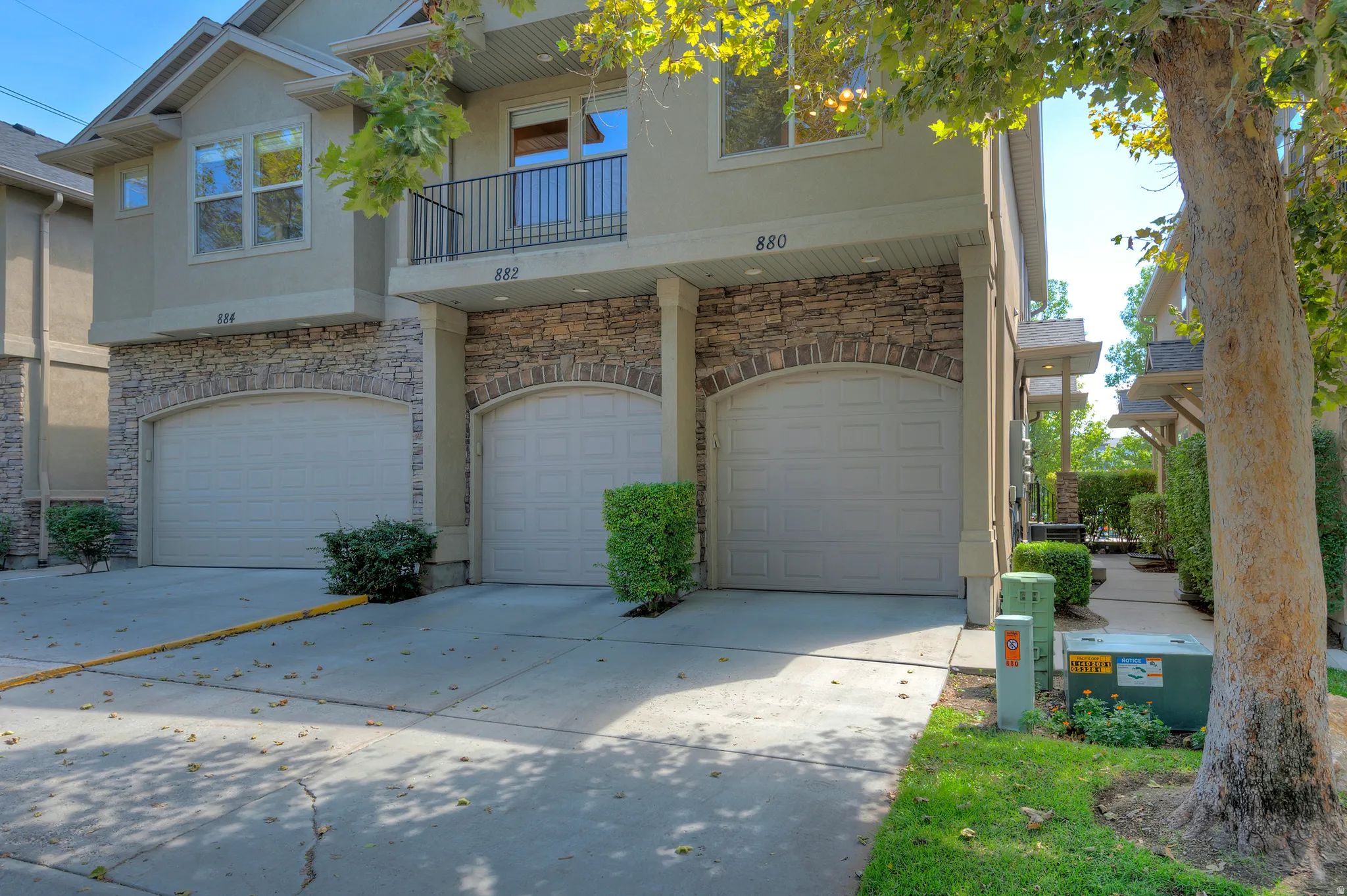 Property exterior featuring stone accents, a private balcony with metal railings, arched garage doors, and mature landscaping