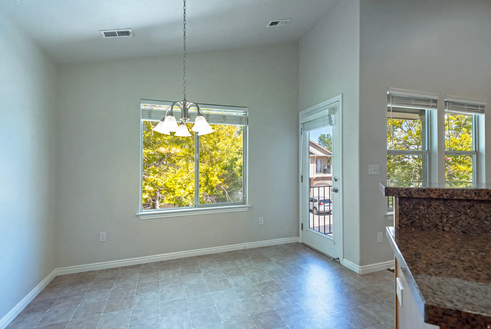 Tiled flooring, vaulted ceiling, multiple windows, built-in lighting, and a glass-paneled door