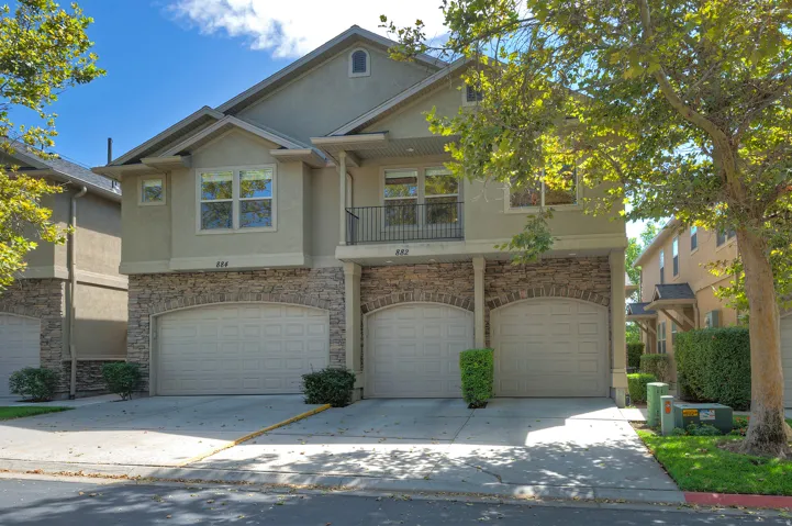Multi-level exterior with stucco and stone veneer, arched garage doors, and an upper-level balcony with metal railing