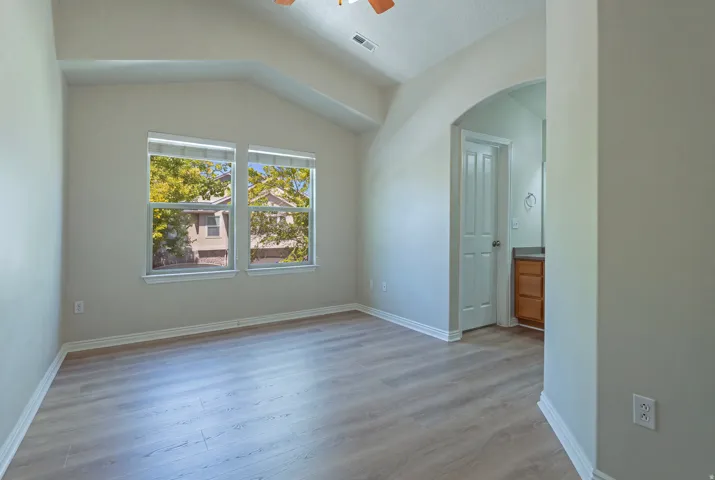 Vaulted ceiling, two large windows, wood-finish flooring, arched doorway, and a vanity with a wood-finish cabinet