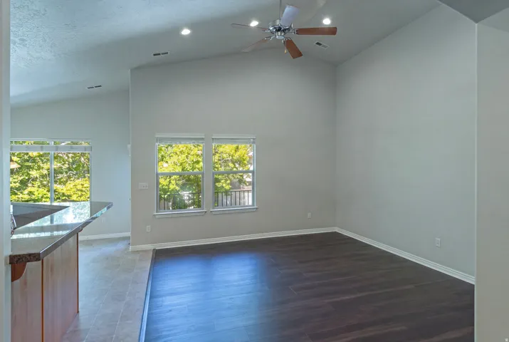Vaulted ceilings, recessed lighting, wood-finish flooring, a ceiling fan, and a built-in breakfast bar with a stone-finish countertop
