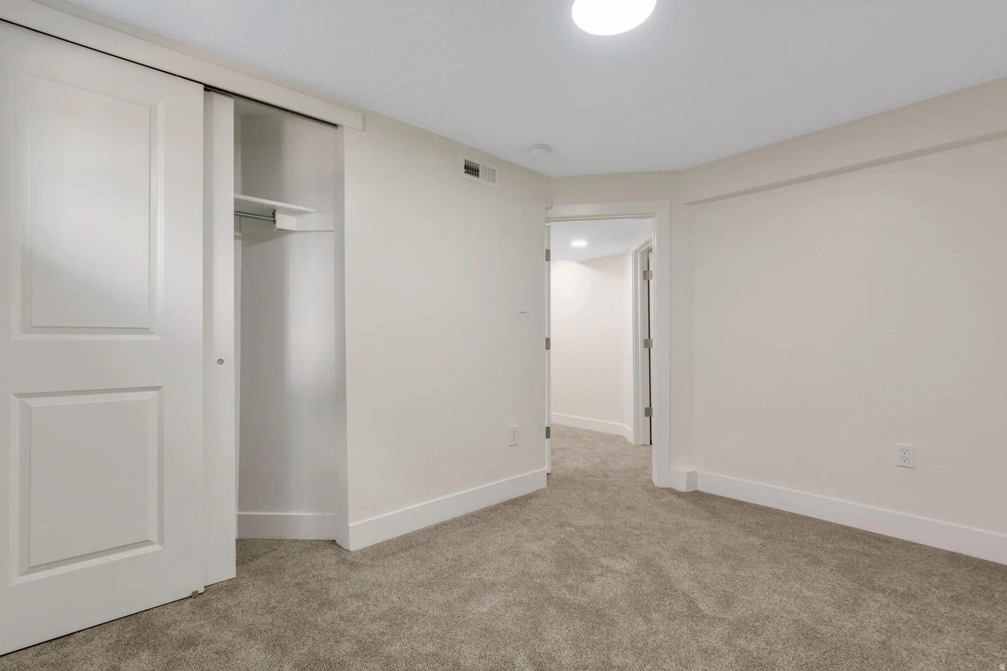 Bedroom 6 - Neutral tone wall paint, white trim, recessed lighting, carpet flooring, and a sliding closet door with built-in shelving