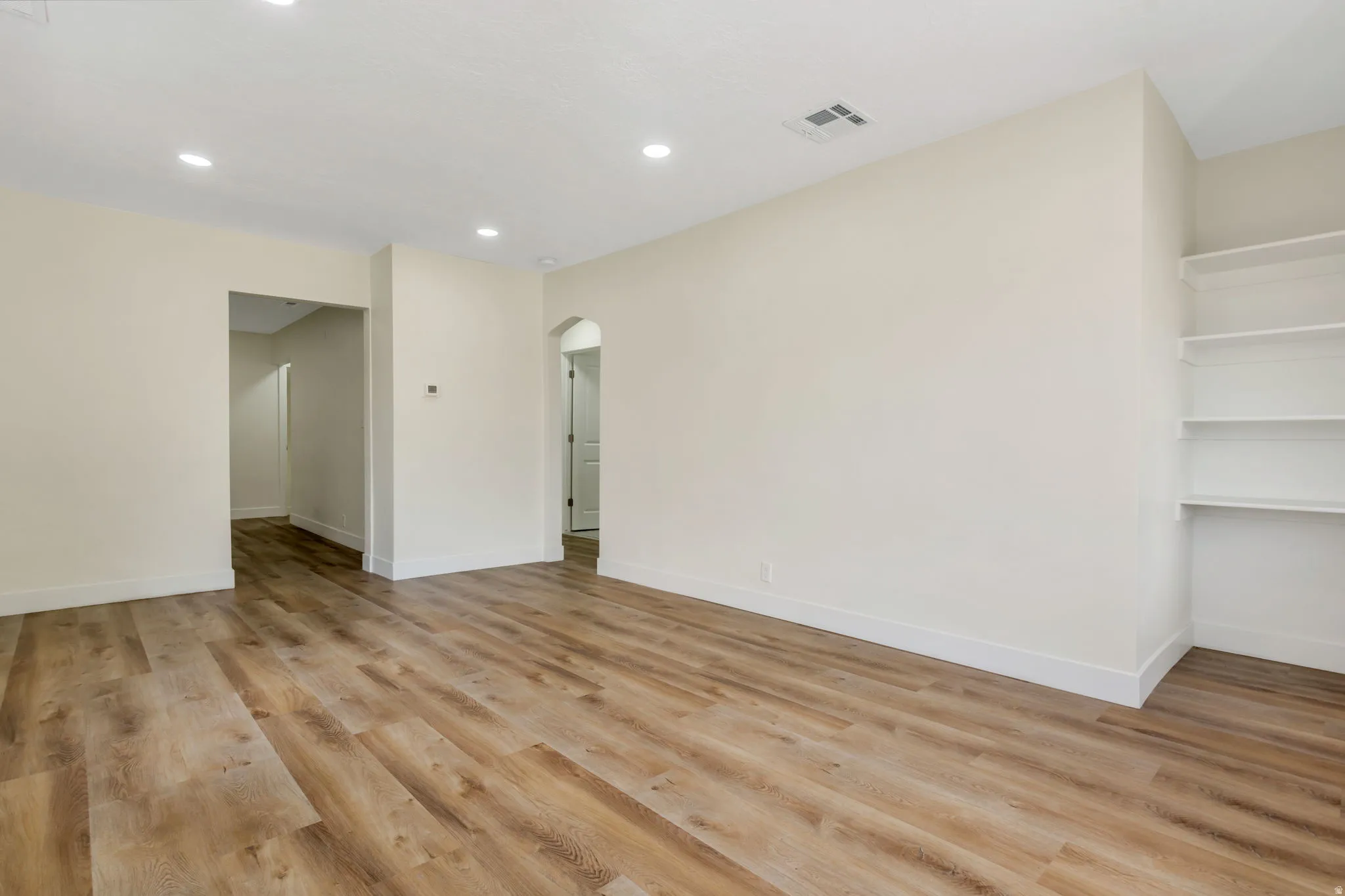 Recessed lighting, LVP flooring, built-in shelving, and an arched doorway