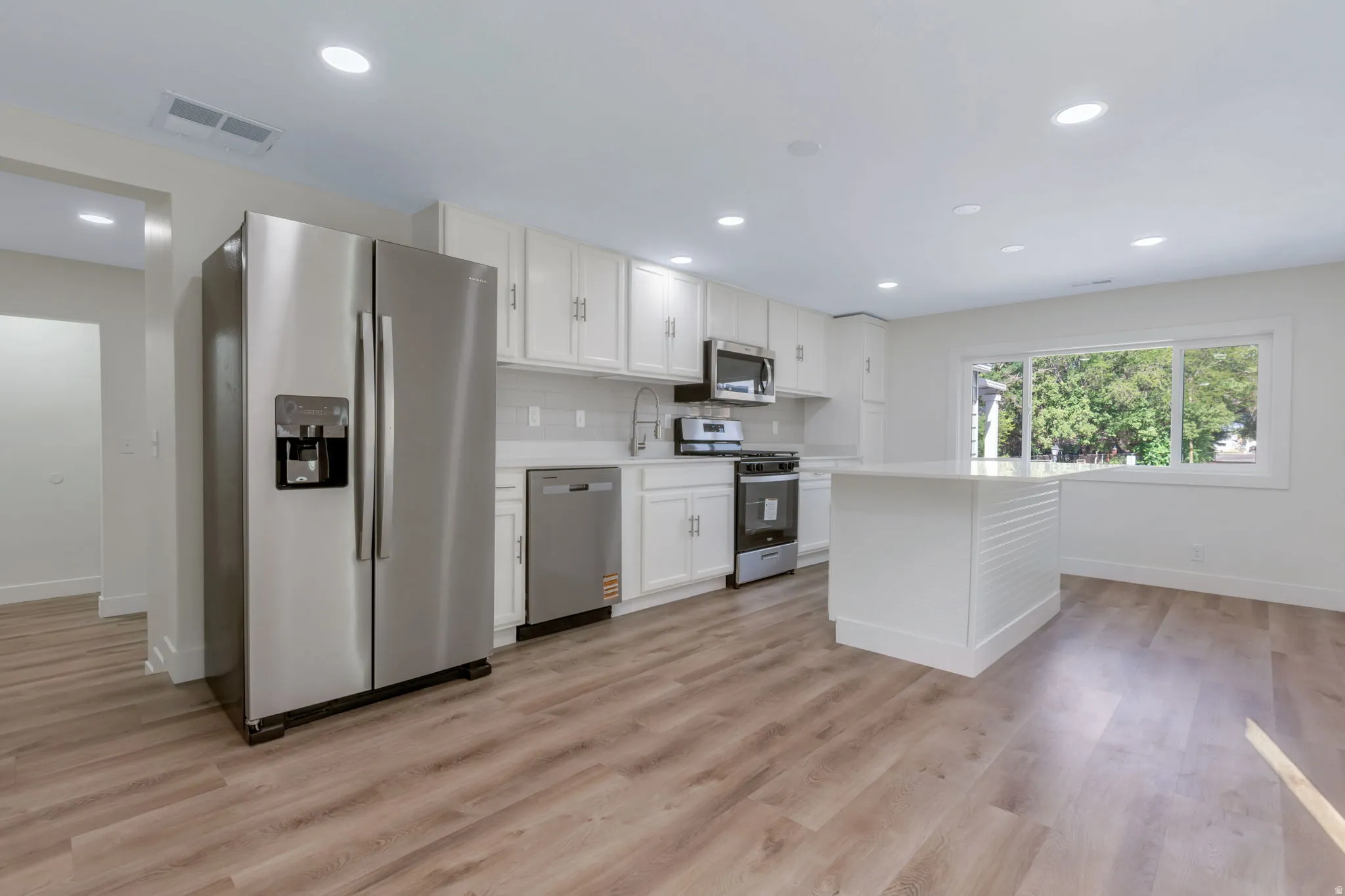 Kitchen featuring LVP flooring, white cabinetry, stainless steel appliances, a center island, and recessed lighting