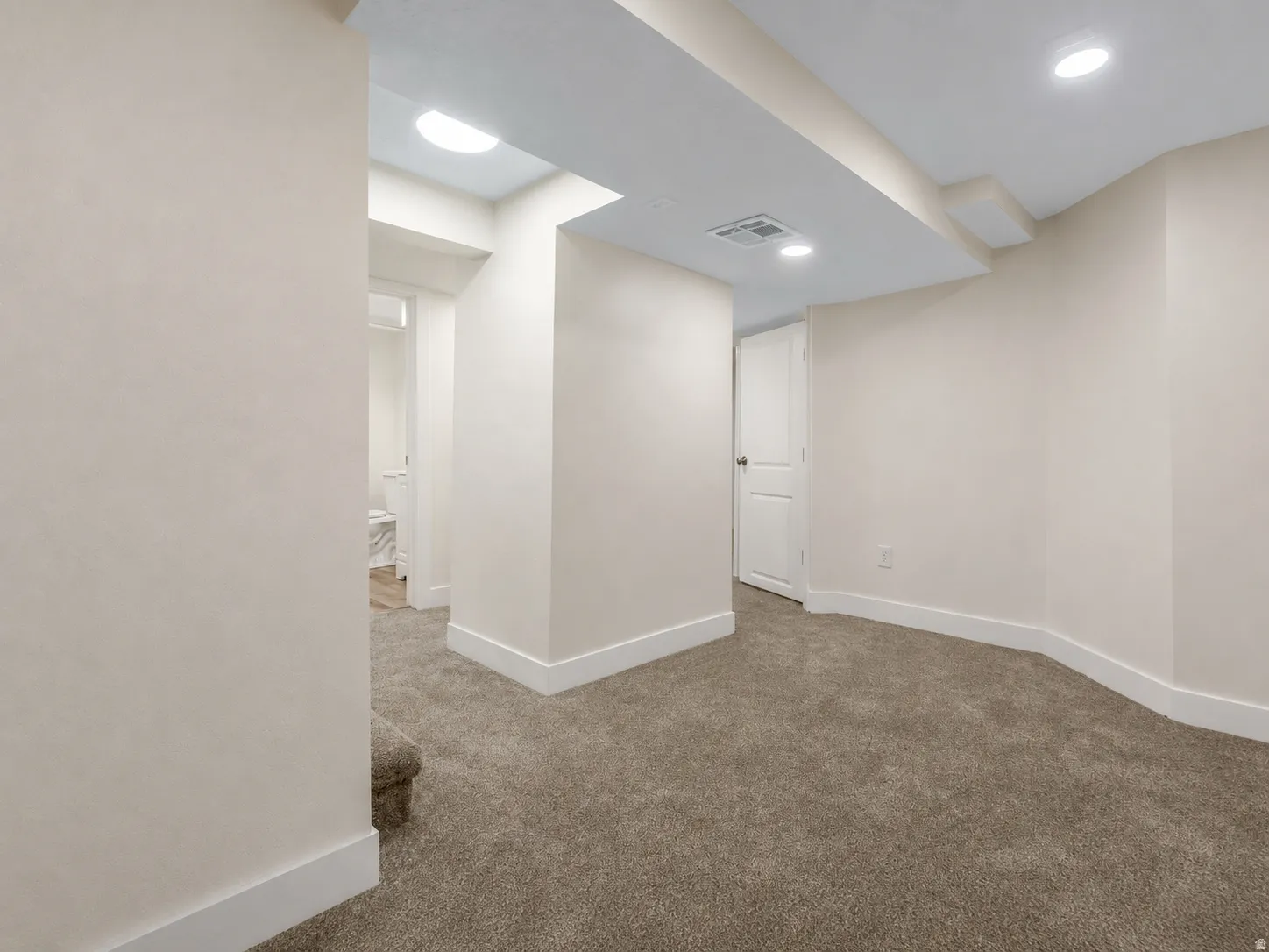 Recessed lighting illuminates the carpeted flooring and light-toned walls, enhancing the neutral interior