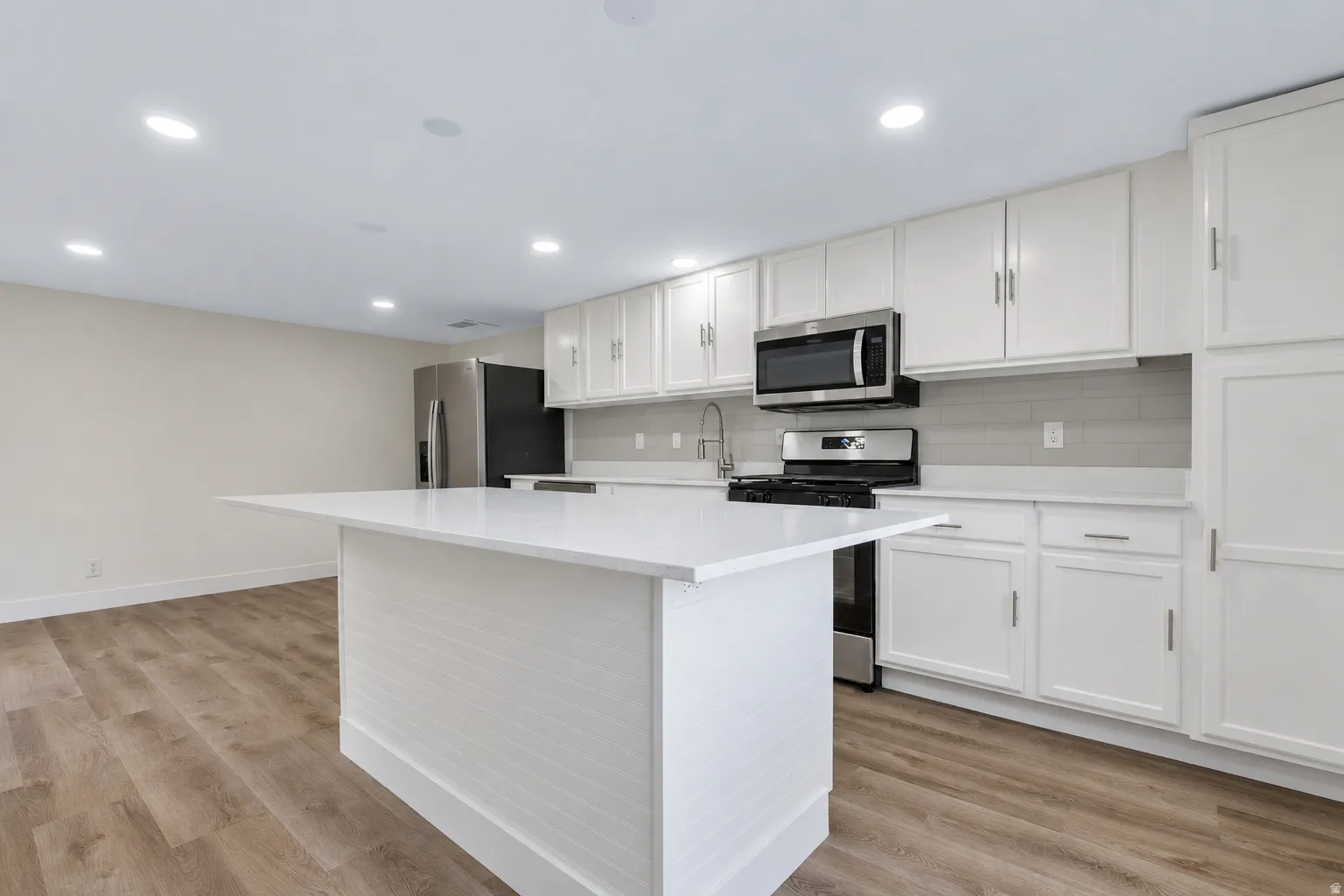 Kitchen featuring an island with a light-colored countertop, white cabinetry, integrated stainless steel appliances, and LVP flooring