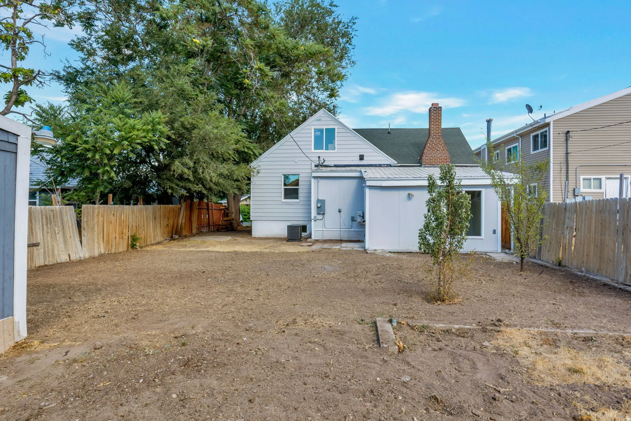 Expansive yard space with a wood privacy fence, a detached shed, and a rear house exterior featuring a brick chimney and vinyl siding