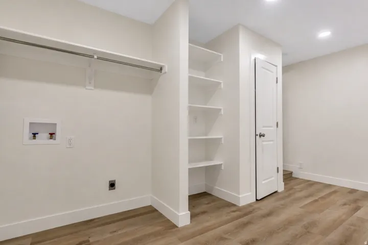 Dedicated laundry area with hookups, overhead shelving, LVP flooring, recessed lighting, and a solid core door