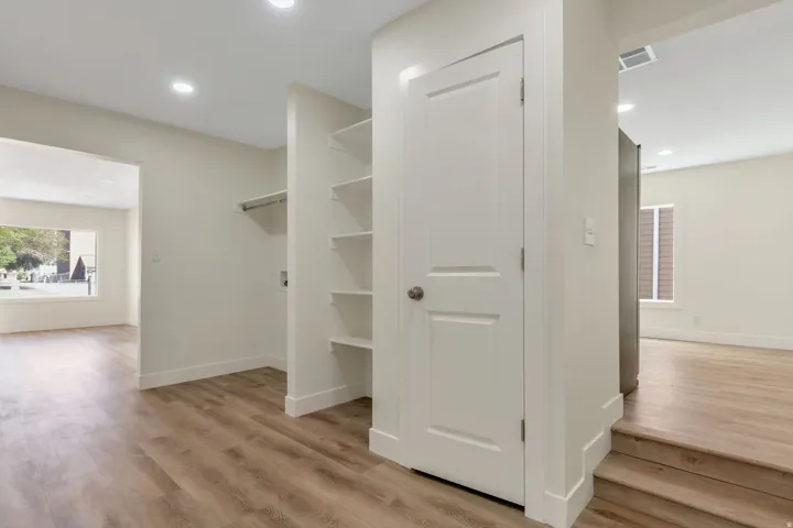 Pantry with door, built-in shelving, wood-finish flooring, recessed lighting, white interior doors, and a stainless steel refrigerator