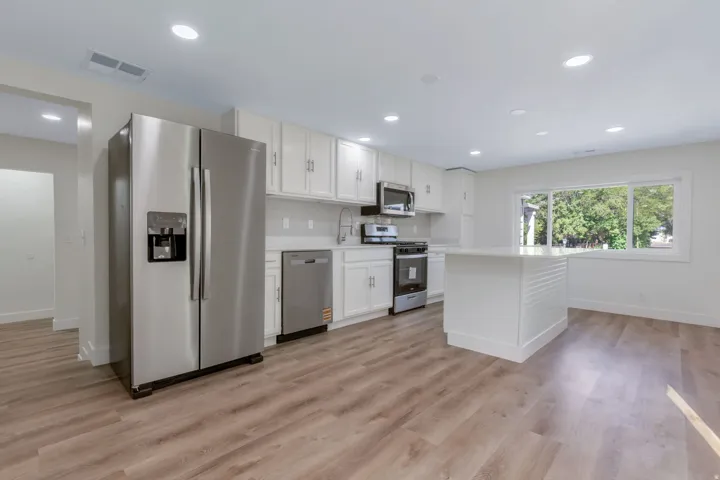 Kitchen featuring LVP flooring, white cabinetry, stainless steel appliances, a center island, and recessed lighting