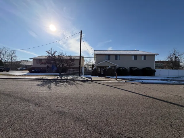 Two-story building with a covered entryway, a white privacy fence, and paved parking