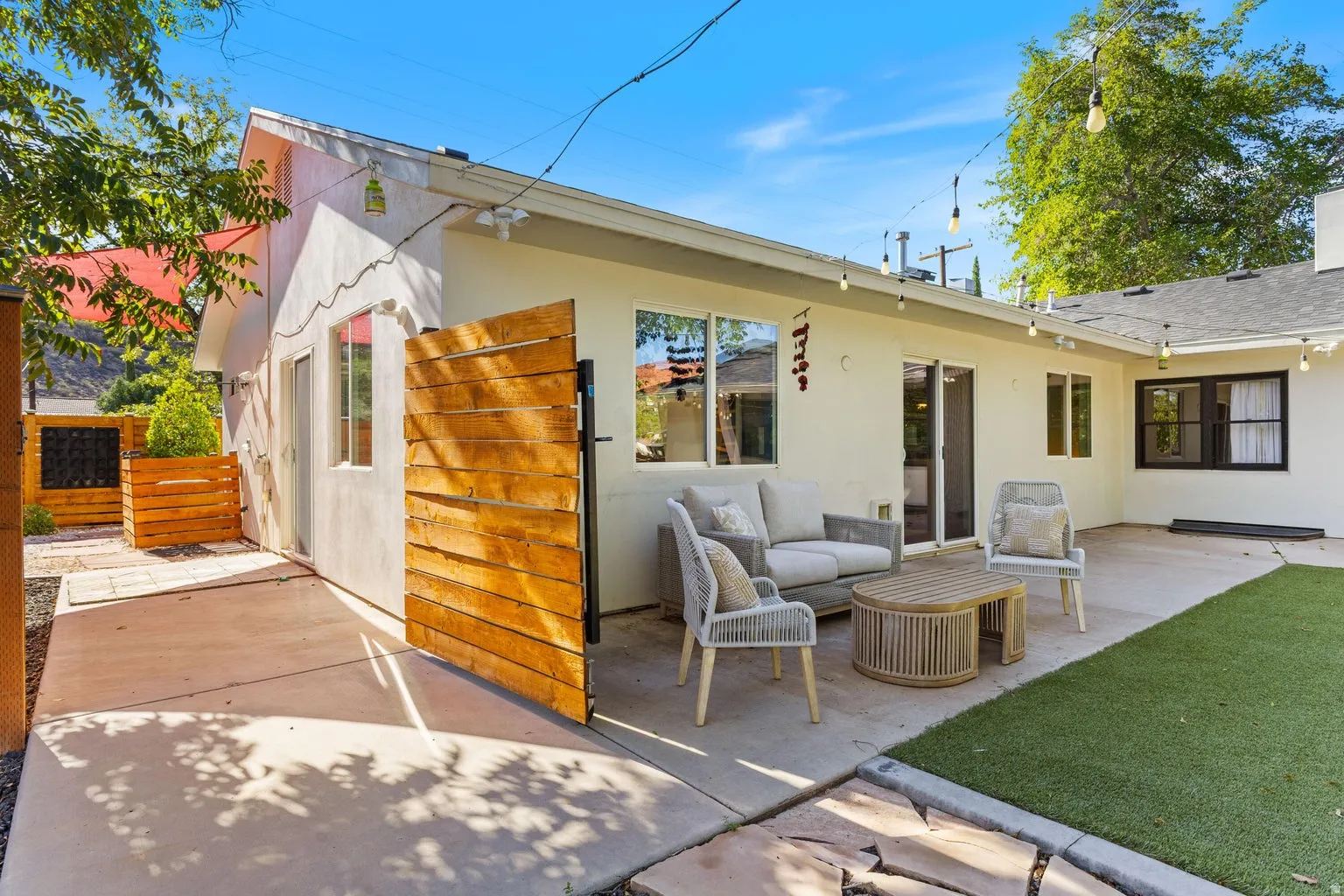 Expansive concrete patio with synthetic turf lawn, featuring sliding glass doors and multiple windows