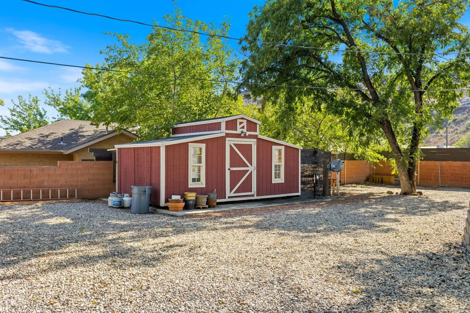 Gravel-covered yard featuring a red storage shed with white trim, a mature tree, and a block wall perimeter