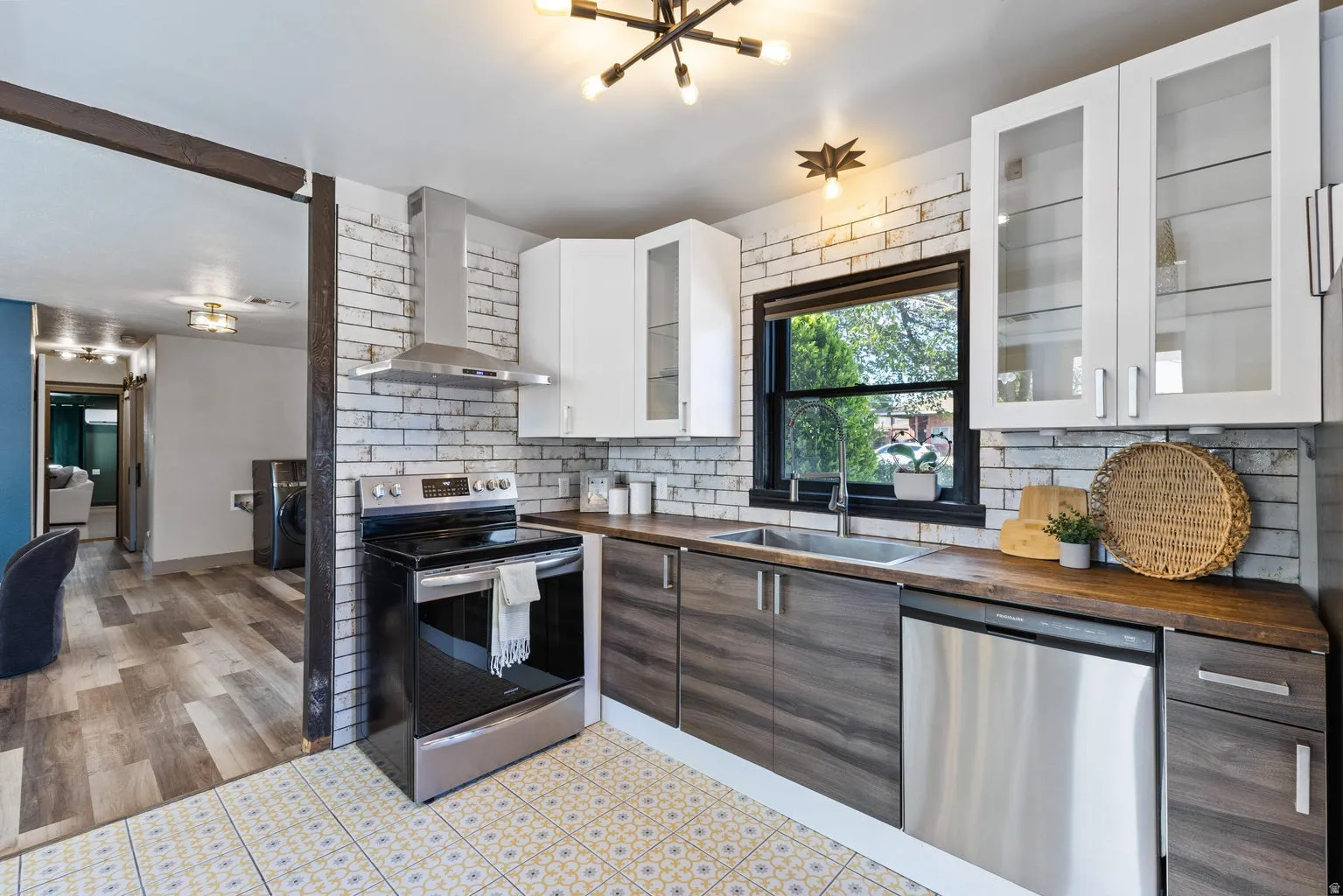 Contemporary kitchen featuring patterned floor tiles, a white brick-style backsplash, stainless steel appliances, wood-finish countertops, and white upper cabinetry with glass inserts