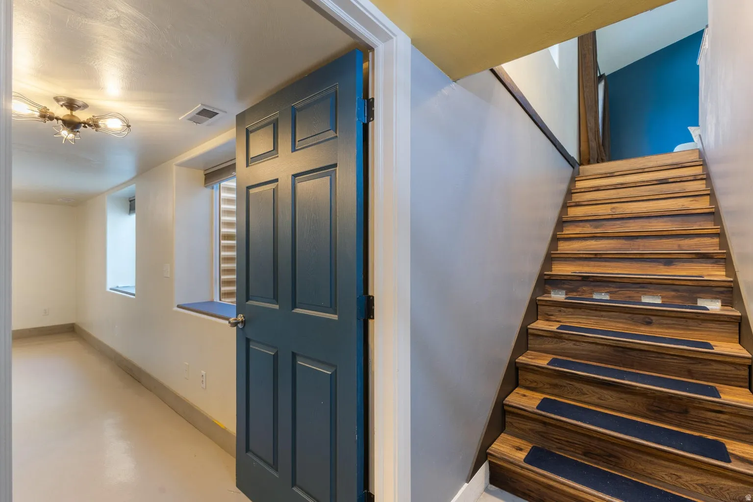 Wood-finish staircase with risers, paneled door, flush-mount ceiling fixture, and deep window sills