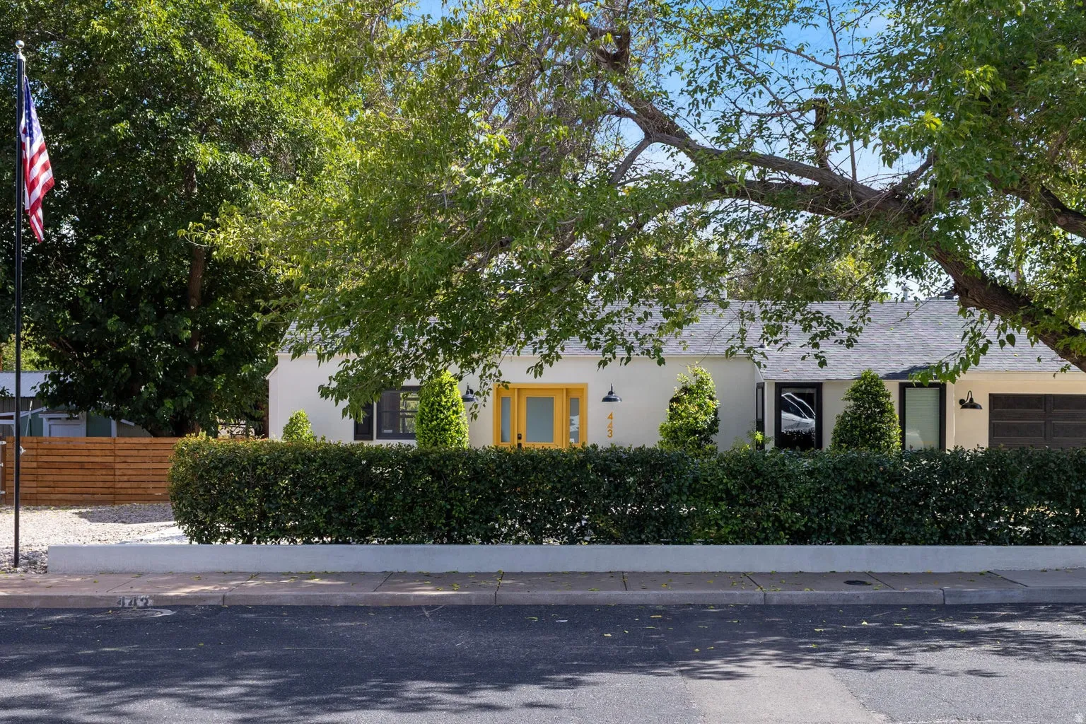 White stucco exterior with a gray shingled roof, featuring a vibrant yellow front door and black garage door