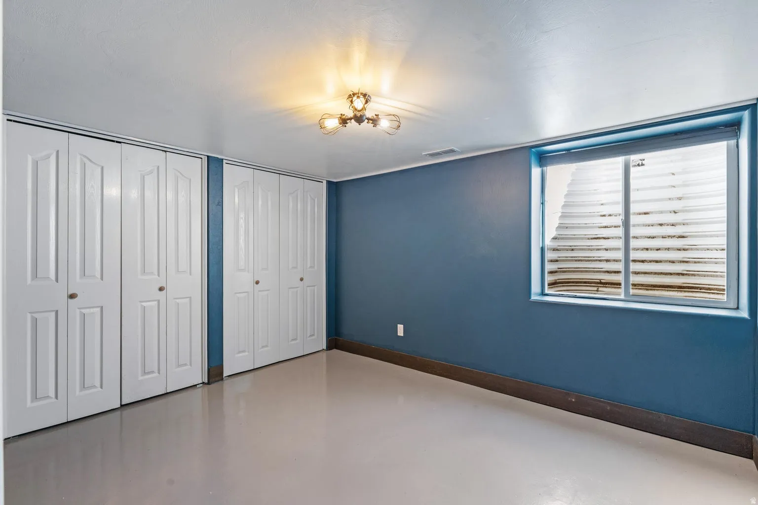 Recessed window with white blinds, dual bi-fold closet doors, and ceiling-mounted light fixture