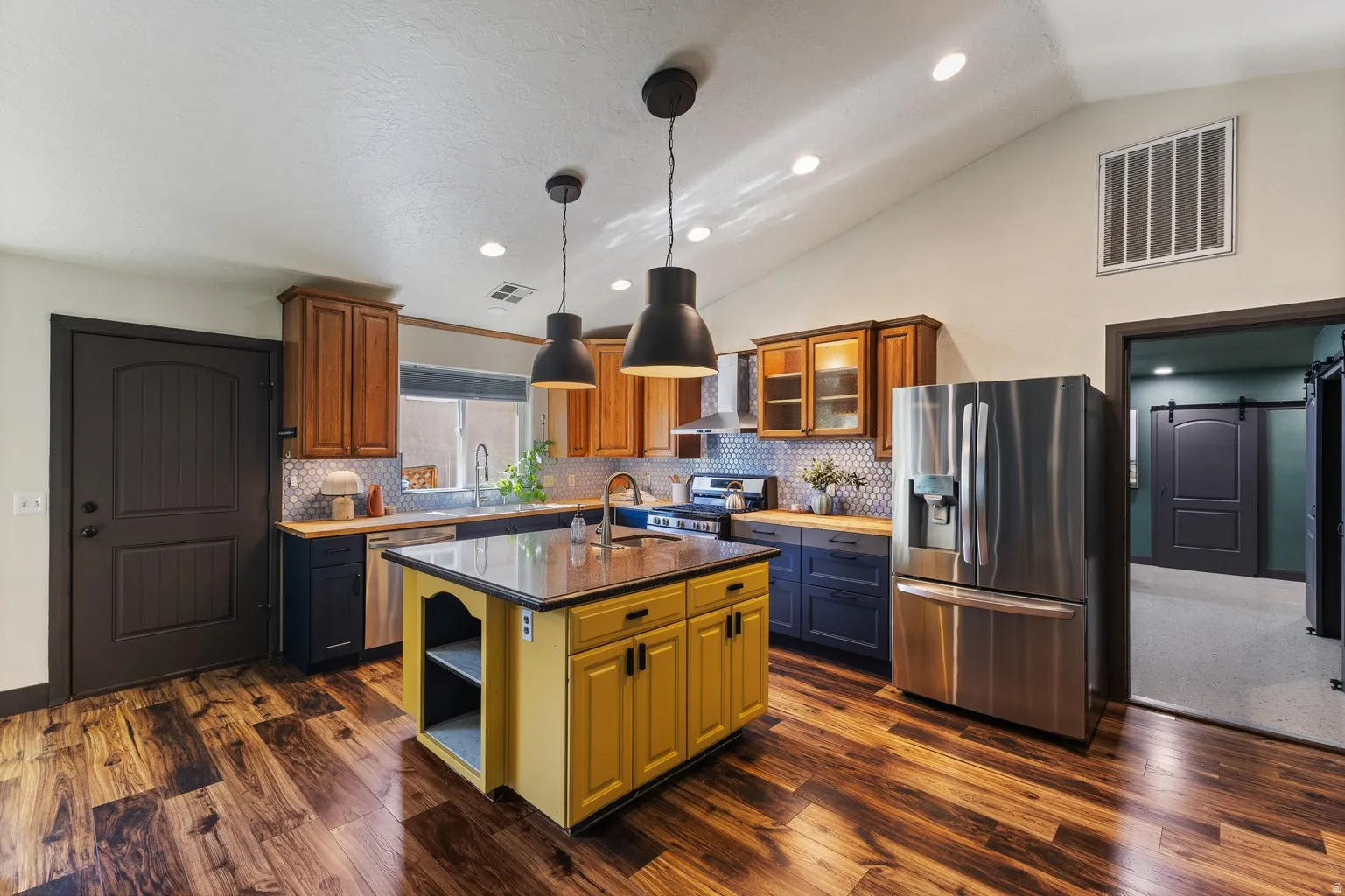Kitchen featuring wood-finish flooring, vaulted ceiling, stainless steel appliances, and a central island with a solid surface countertop