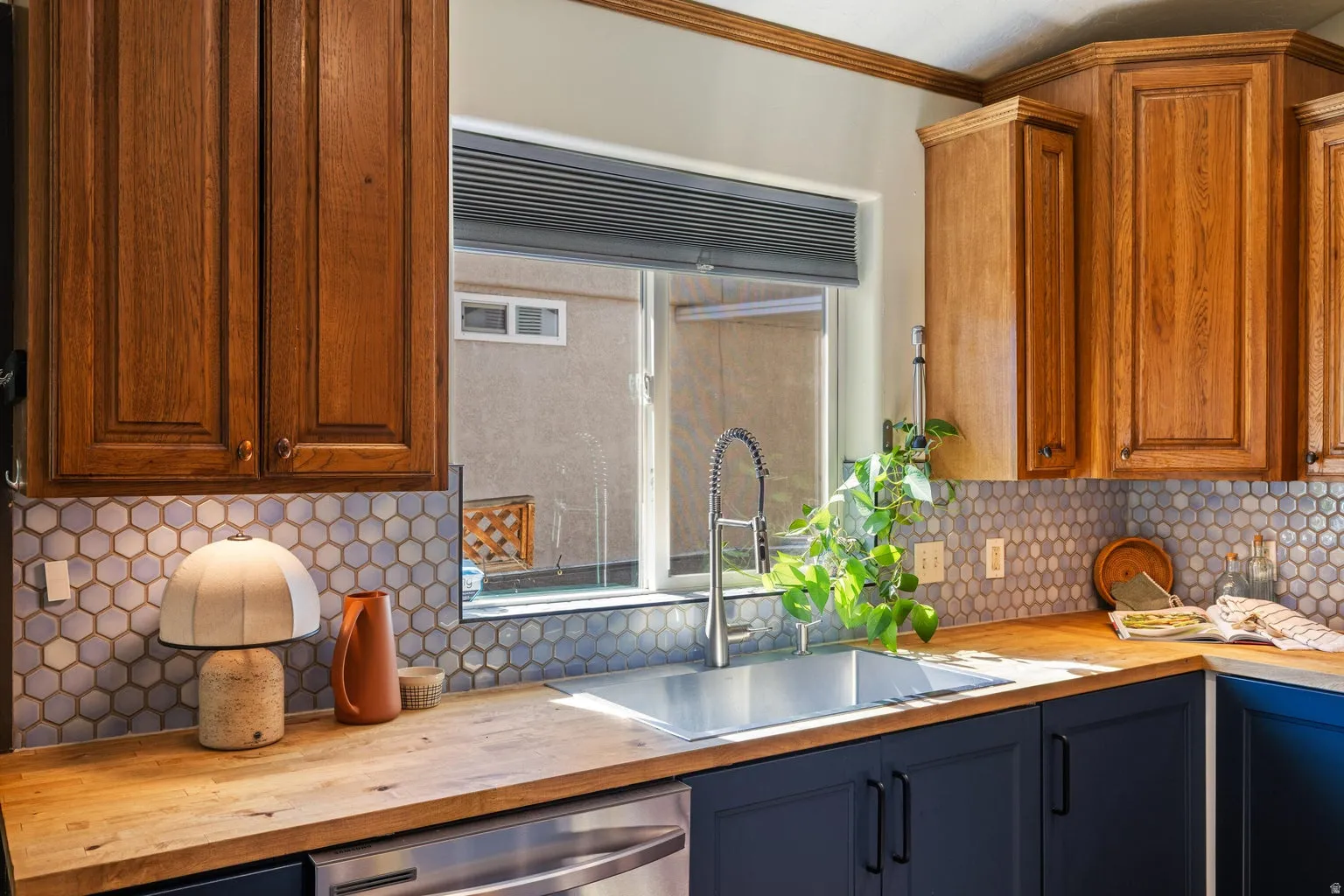 Stainless steel sink with a gooseneck faucet, light wood-finish countertops, two-tone cabinetry, and a hexagonal tile backsplash