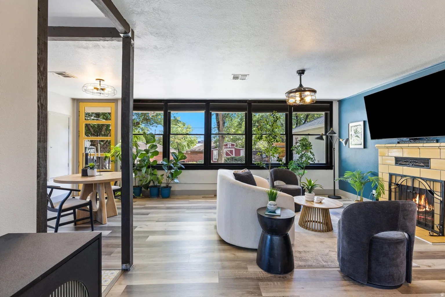 Living area featuring wood-finish flooring, a fireplace with a light-colored tiled surround, a built-in wall-mounted television, and a ceiling fan with integrated lighting