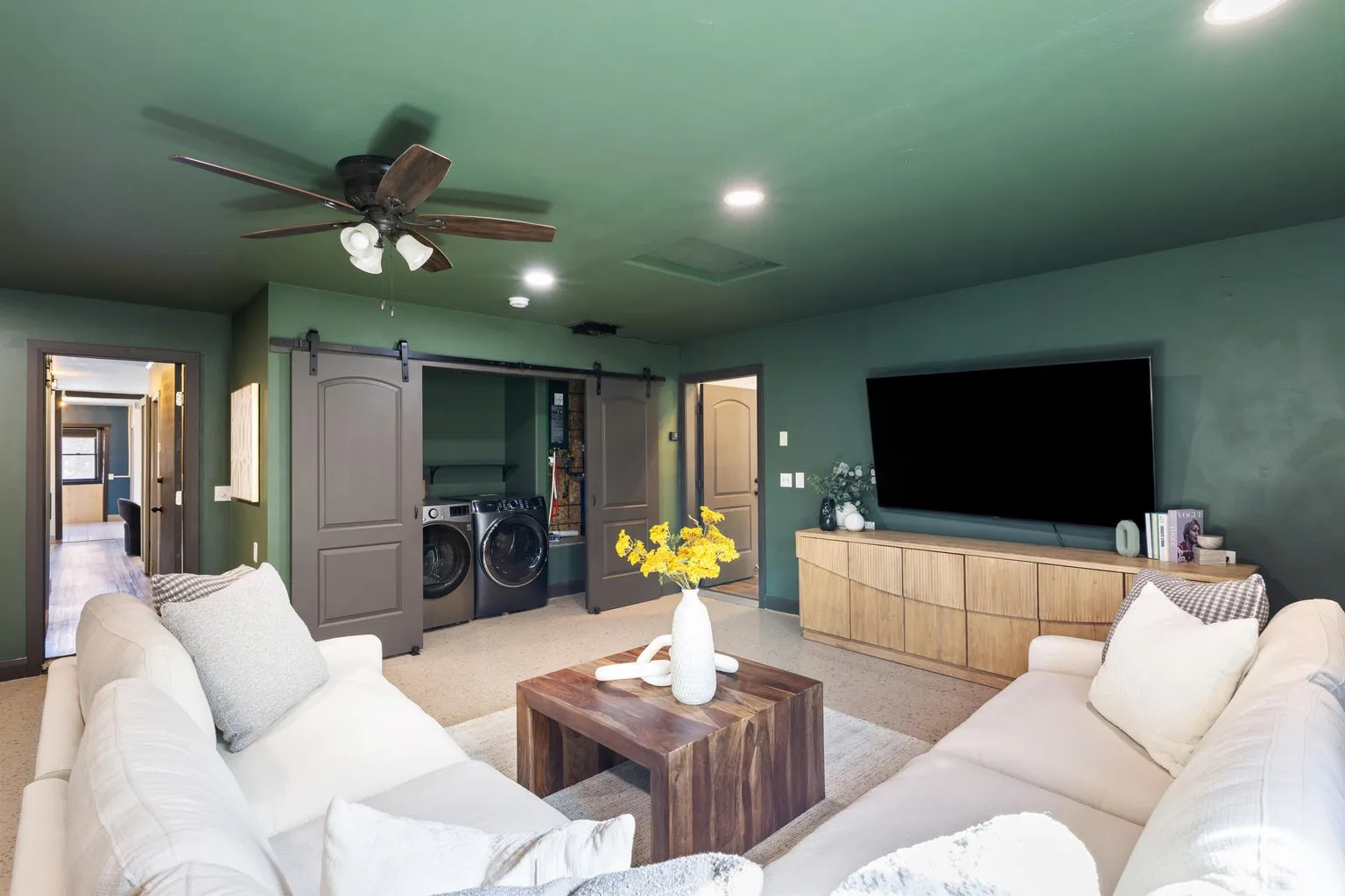 Integrated laundry area with sliding barn doors, a wood-finish media console, recessed lighting, and a ceiling fan