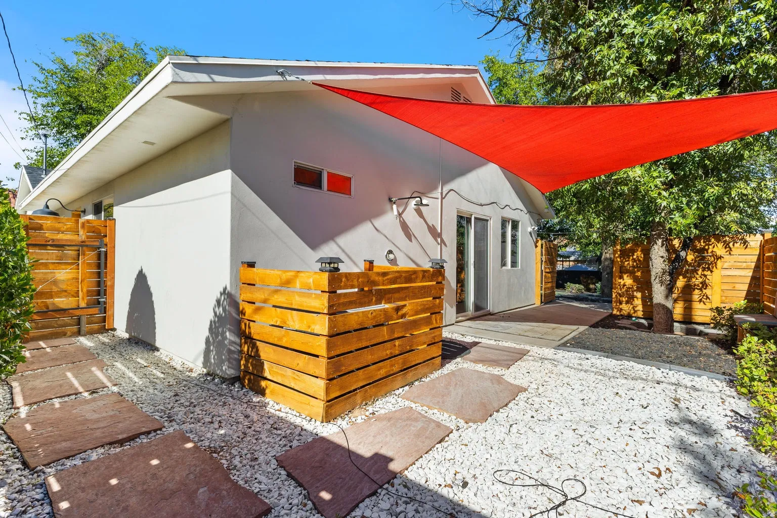 Exterior featuring white gravel, flagstone pavers, wooden privacy fencing, a red shade sail, and a sliding glass door
