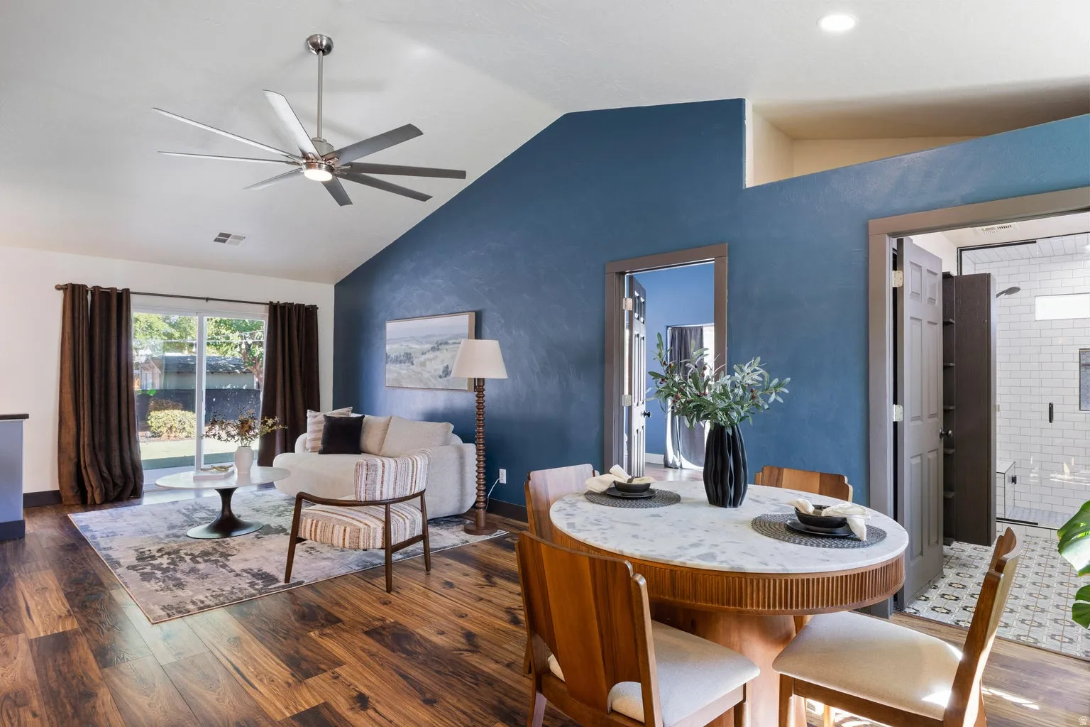 Vaulted ceiling with an installed ceiling fan, wood-finish flooring, sliding glass patio door, and accent wall