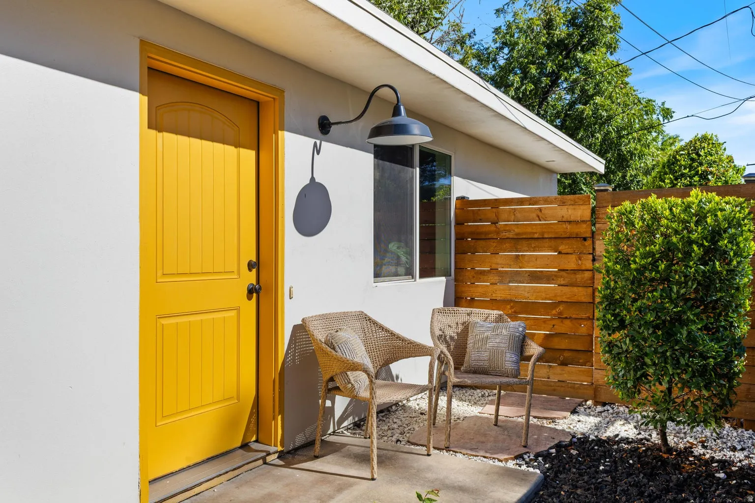 Exterior featuring a brightly painted entry door, wall-mounted light fixture, and a slatted wood privacy fence