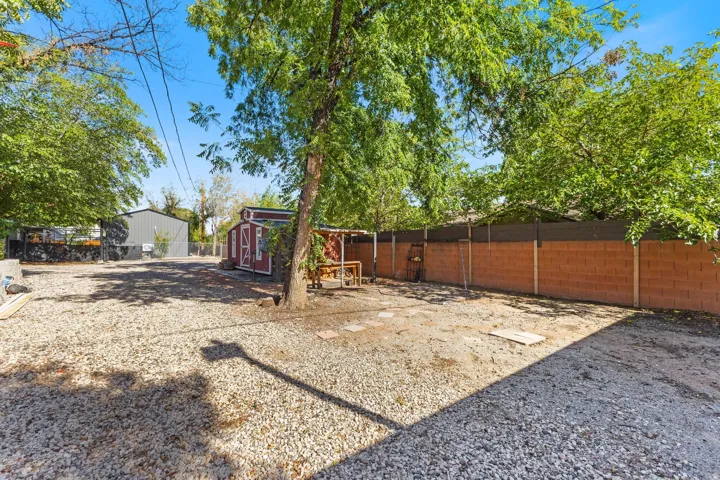 Expansive gravel-covered yard featuring a red storage shed, mature trees, and a block perimeter wall