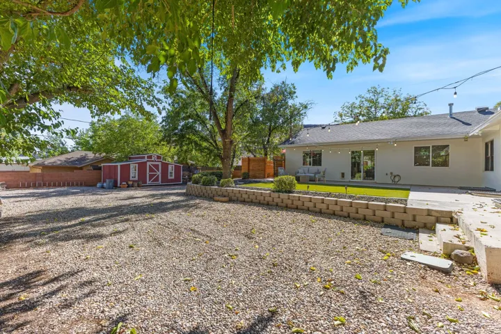 Expansive backyard featuring a gravel area, a red storage shed, a raised planter bed with block retaining wall, a concrete patio, and a section of artificial turf