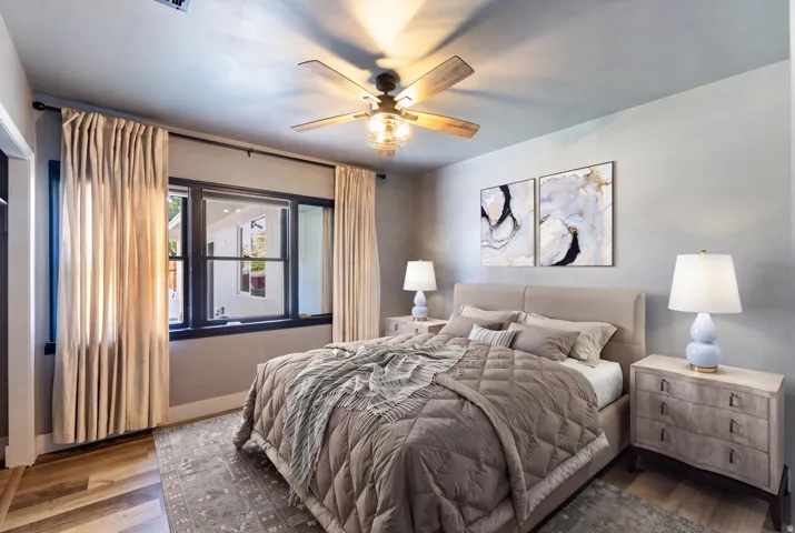 Wood-finish flooring with a neutral paint palette, featuring a ceiling fan with integrated lighting and a window with dark trim
